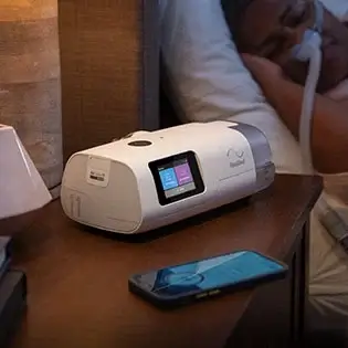 Het AirCurve 11 ASV PaceWave-apparaat op een nachtkastje terwijl de gebruiker slaapt, met een mobiele telefoon ernaast.