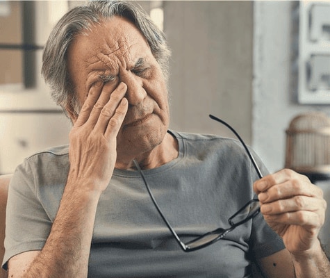  Een oudere man die in zijn oog wrijft en er moe uitziet.